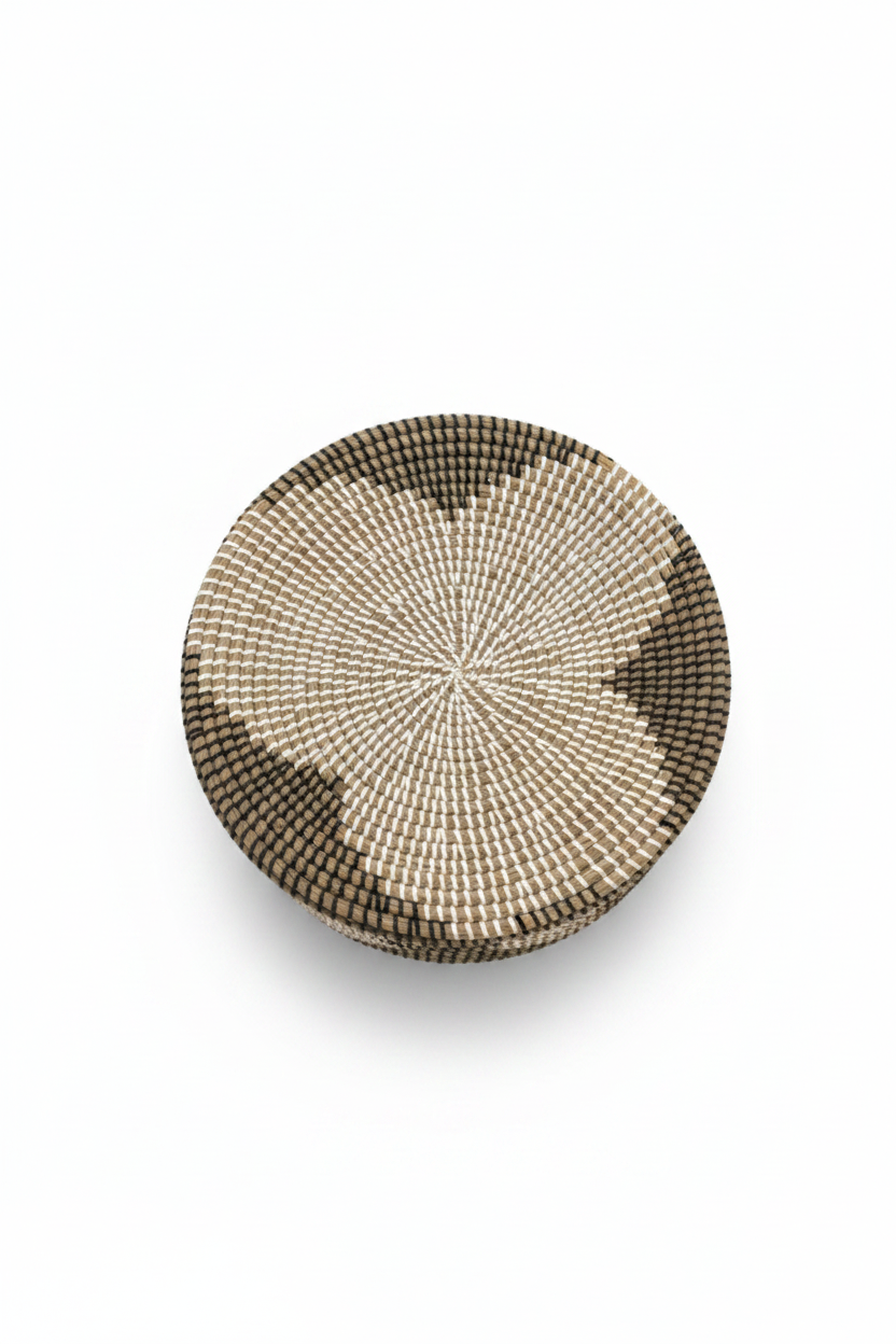 Vue du dessus du couvercle plat en jonc tressé, motif spirale concentrique crème et noir, panier artisanal africain, fond blanc