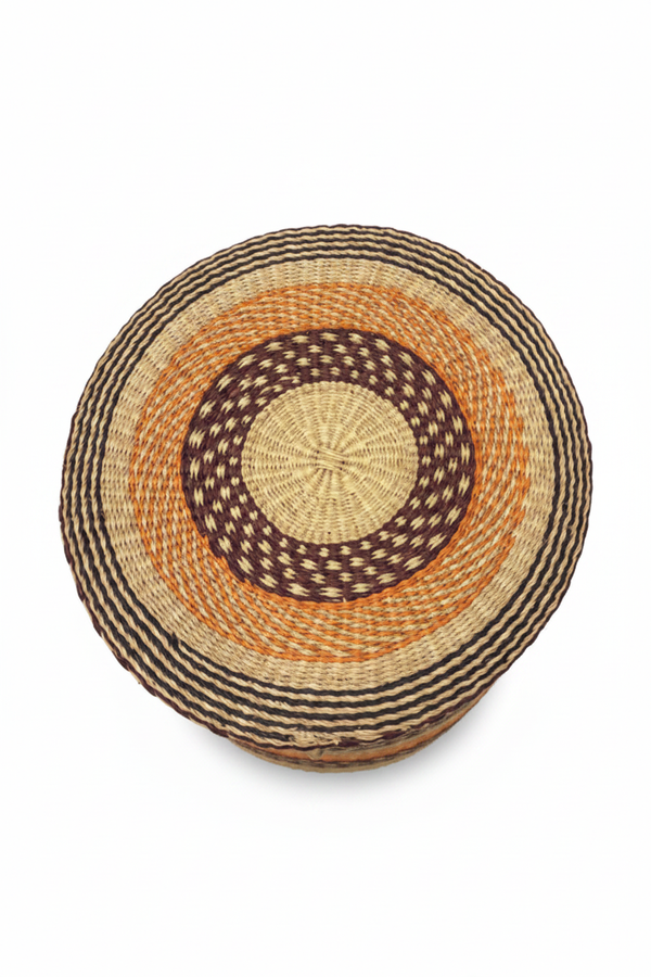 Panier artisanal africain tressé vu de dessus — couvercle rond avec motif spirale concentrique en raphia naturel, orange et brun foncé, fond blanc
