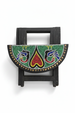 Tabouret pliant africain en bois ébénisé noir avec panneau semi-circulaire orné de perles multicolores motifs traditionnels représentant deux oiseaux stylisés sur fond vert, cœur central rouge et jaune, incrustations de triangles en laiton. Fond blanc studio.
